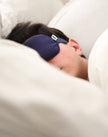 Person sleeping with a blue sleep mask on, lying on a white pillow.