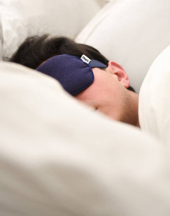 Person sleeping with a blue sleep mask on, lying on a white pillow.