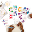 Colorful cards on a white surface with a person writing in a notebook.